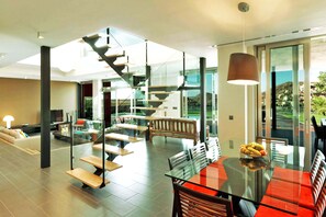 Ein modernes Interieur mit einem Glastisch, roten Sitzgelegenheiten, einer Treppe und Blick auf einen Hügel.