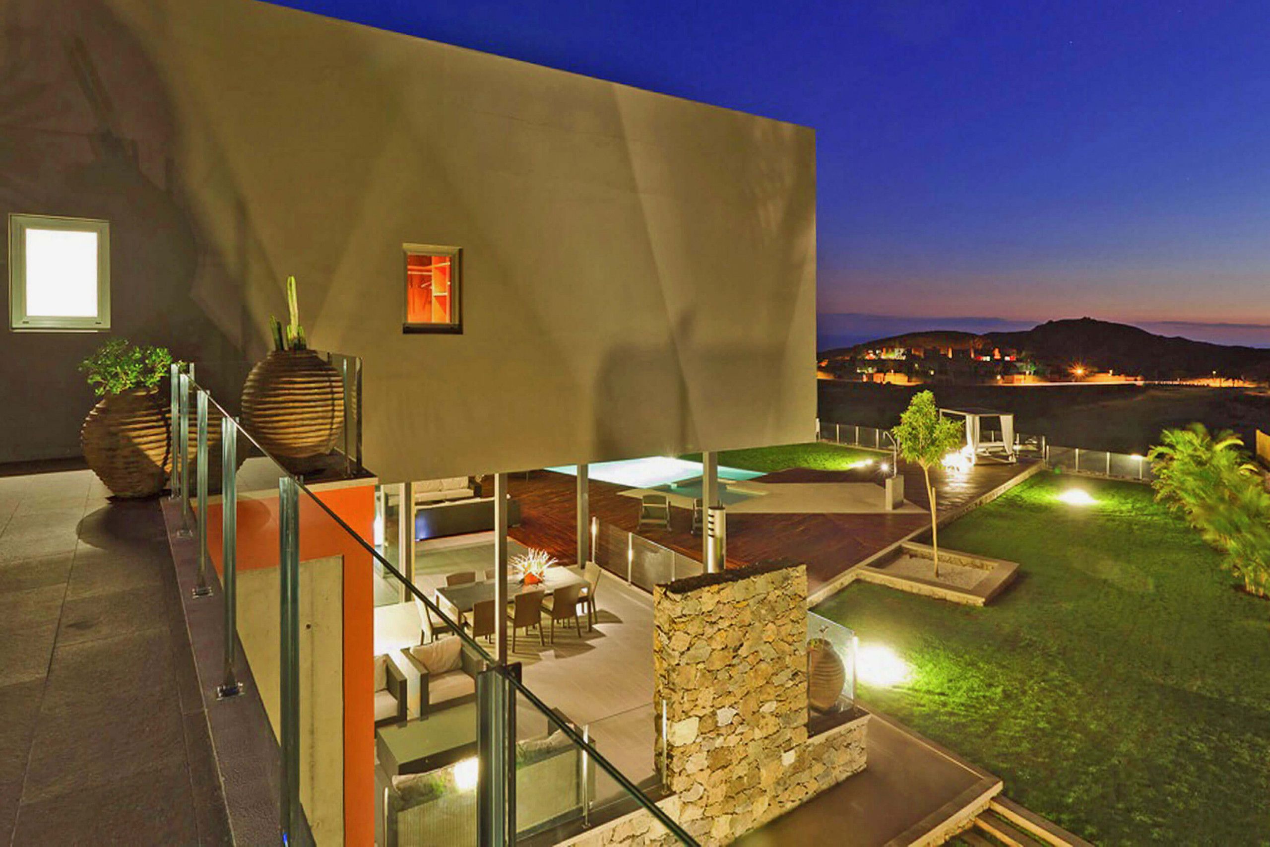 Un patio moderno al aire libre con barandilla de vidrio, pared de piedra y zona de piscina.