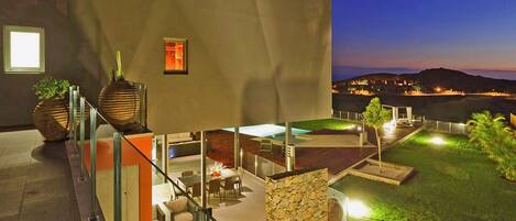 A modern outdoor patio with a glass balustrade, a stone wall, and a pool area.