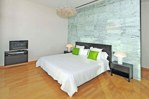 Un dormitorio moderno con una cama grande, televisor y pared de mármol.