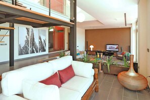 Un salon moderne avec un canapé blanc, des coussins rouges, un téléviseur et des plantes décoratives.