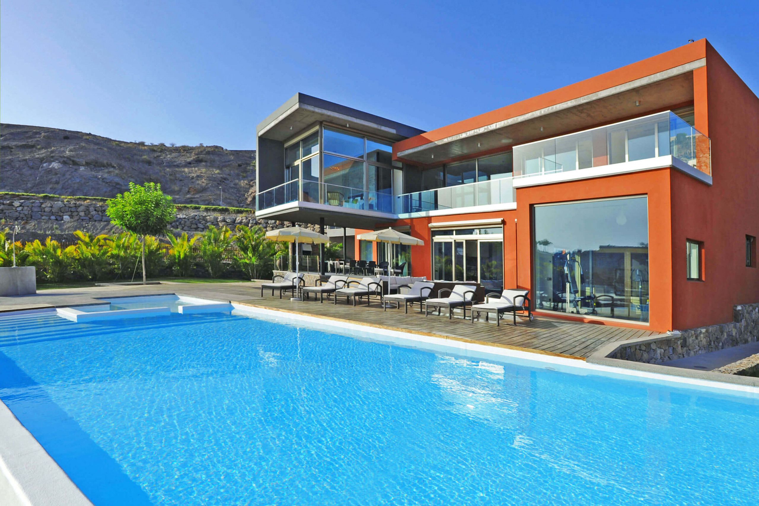 A modern hotel with a pool, outdoor seating, and a mountain backdrop.