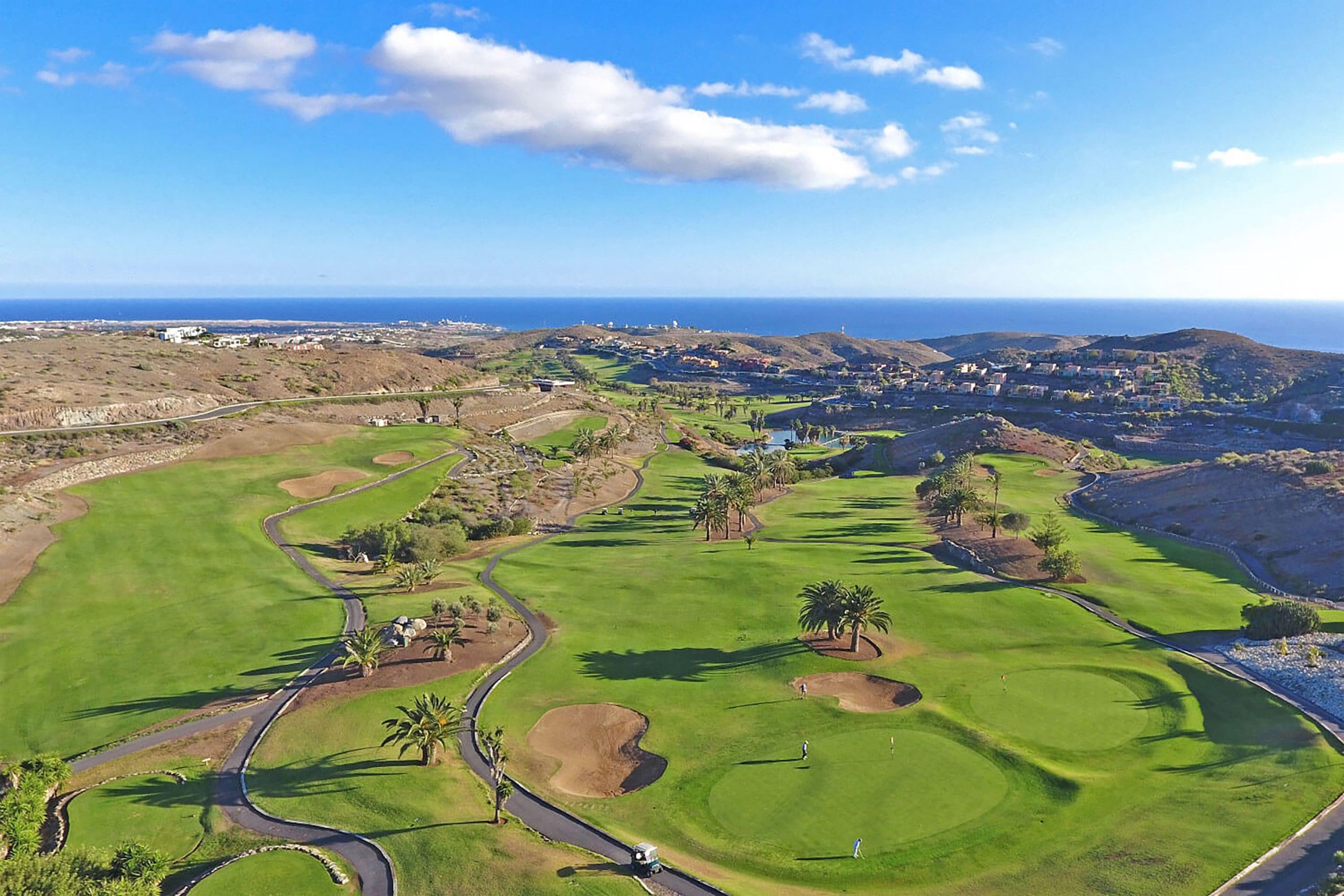 Campo de golf con vista despejada al océano y colinas lejanas.