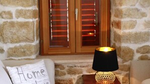 A cozy room with a stone wall, a wooden cabinet with blinds, a striped sofa, and a small table with a lamp.