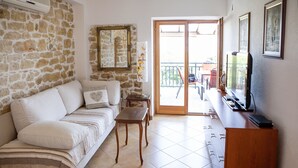 A living room with a stone wall, a sofa, a TV, and a balcony with outdoor furniture.