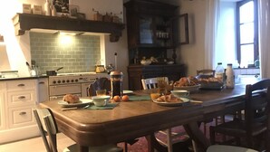 A cozy kitchen with a wooden table set for breakfast, featuring croissants, orange juice, and a coffee maker.