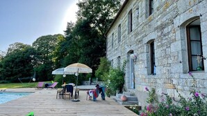 A stone building with a pool area, including lounge chairs and umbrellas.