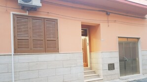 A building with a beige facade, a set of beige steps leading to a door, and a large window with horizontal blinds.