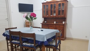 A dining table with a blue tablecloth and wooden chairs, a vase with flowers, and a wooden cabinet with glass doors.