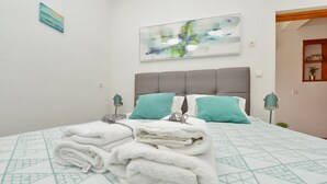 A neatly made bed with a geometric patterned bedspread, two pillows, and a stack of folded towels on the bed. - Apartment Kristijan Sleeps 2 With Wi-fi (Zadar)