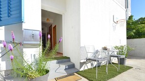 A modern outdoor area with a concrete patio, a small table with chairs, a potted plant, and a door mat. - Apartment Kristijan Sleeps 2 With Wi-fi (Zadar)