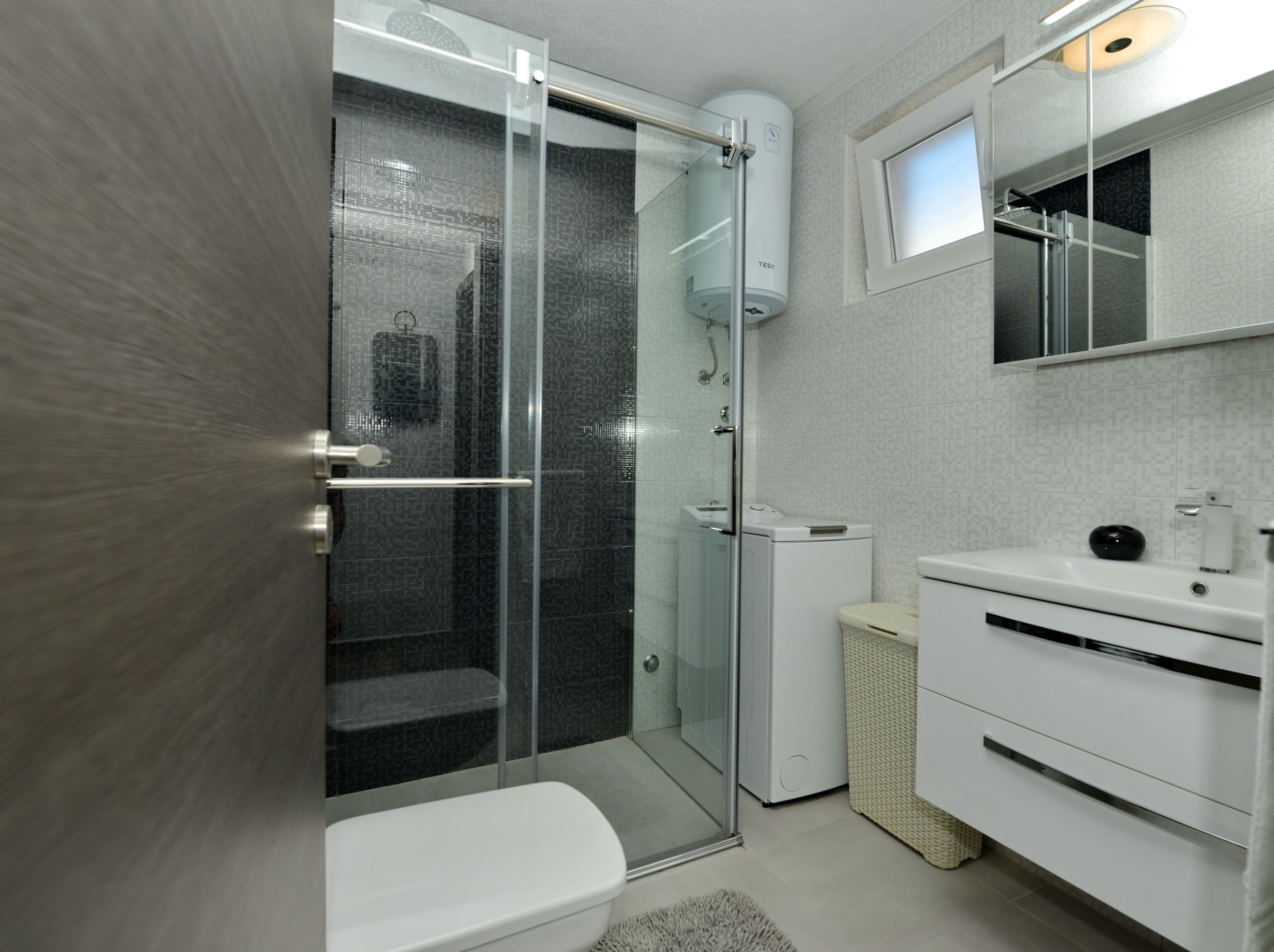 Un baño moderno con ducha de vidrio, inodoro y lavamanos con espejo.