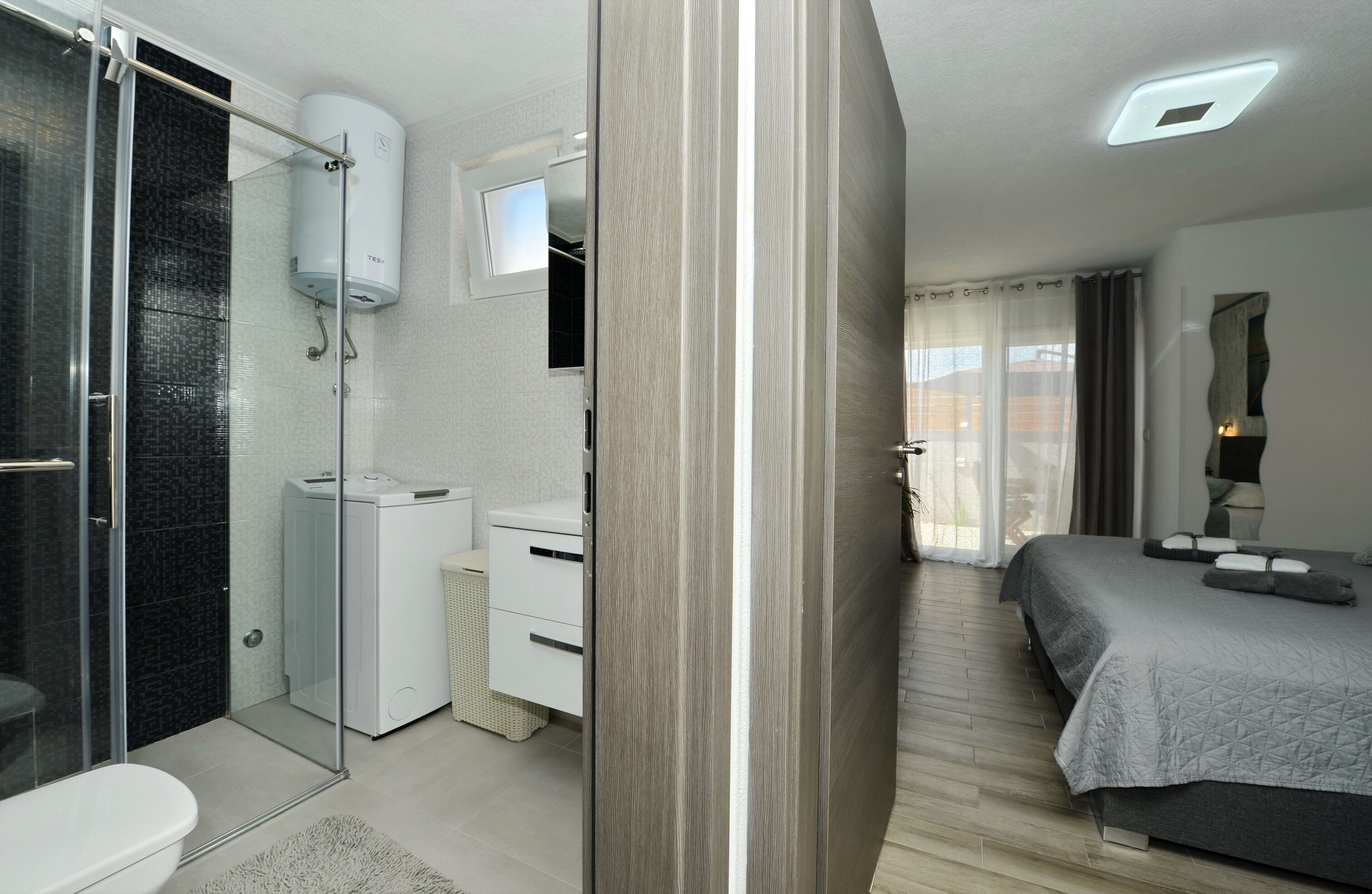 Une chambre d’hôtel moderne équipée d’une douche, de toilettes et d’un lit avec une couette grise.