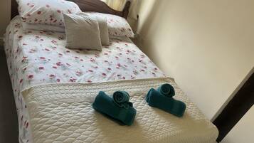 A neatly made bed with floral bedding, two rolled towels, and a quilted cover.