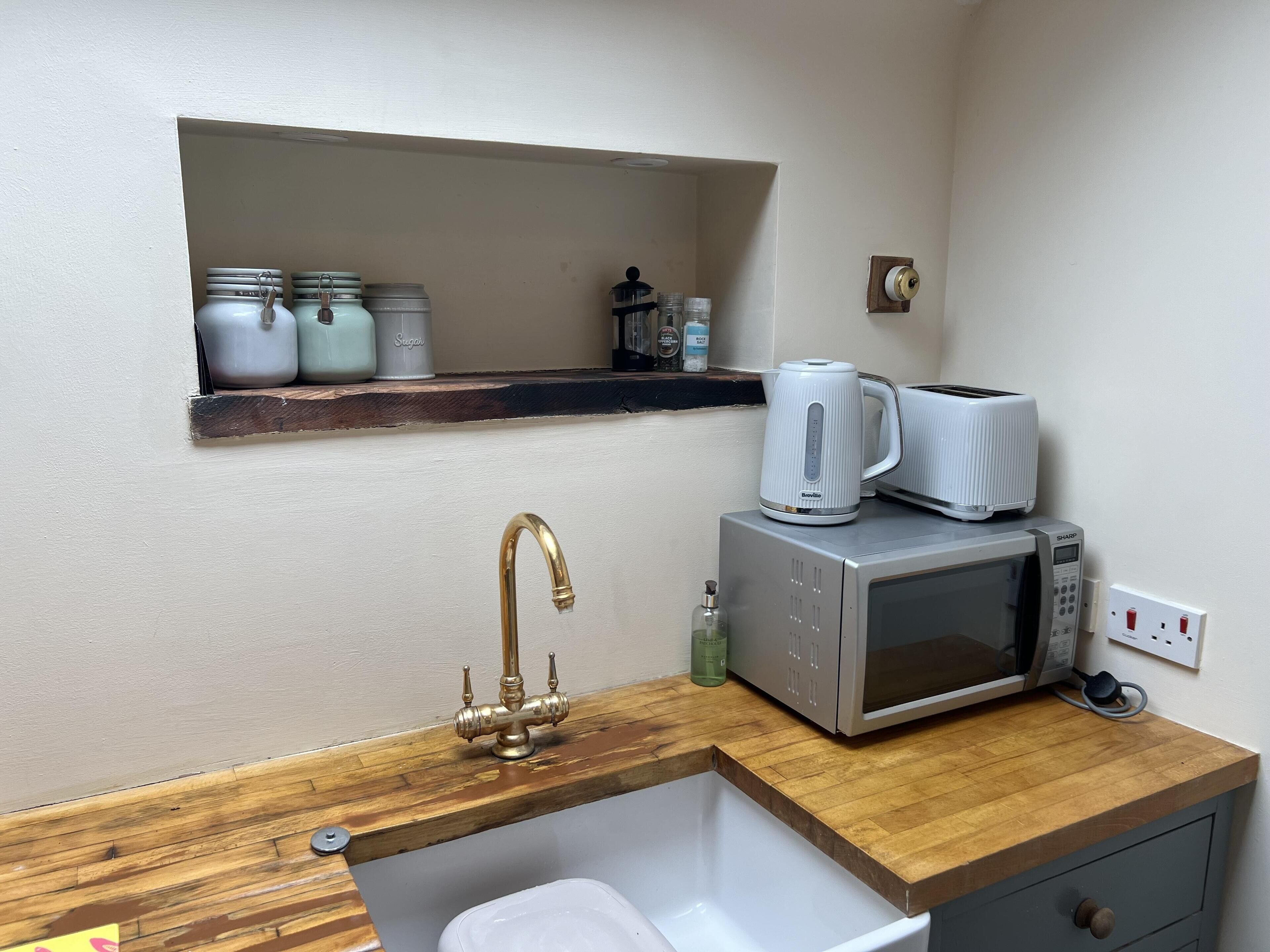 A compact kitchen with a wooden countertop, a stainless steel sink, a white kettle, a toaster, and a microwave.