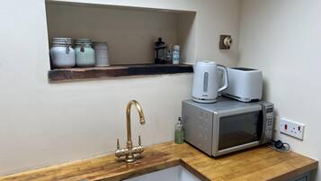 A compact kitchen with a wooden countertop, a stainless steel sink, a white kettle, a toaster, and a microwave.