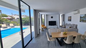 A modern living room with a pool view, a sofa set, a dining table, and a TV.
