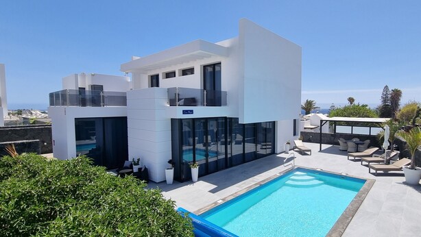 A modern villa with a swimming pool, outdoor seating, and a view of the sea.
