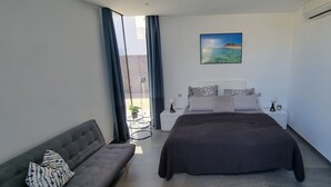 A modern bedroom with a large bed, a sofa, a small table, and a potted plant.