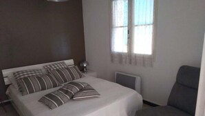 Une chambre à coucher avec un lit, une table de chevet, une lampe, une chaise et une fenêtre.