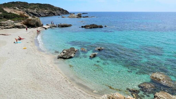 Une plage à l’eau turquoise et limpide, avec des rochers et quelques personnes.