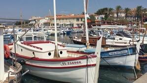Un port de plaisance avec plusieurs bateaux amarrés, un ciel dégagé et des bâtiments en arrière-plan.