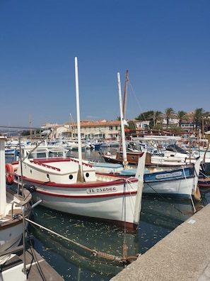 Una marina con varios barcos amarrados, cielo despejado y edificios al fondo.