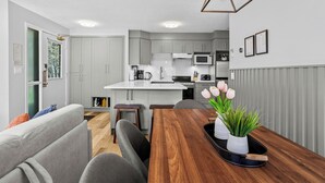 Una cocina moderna con gabinetes grises, una encimera blanca y una mesa de comedor de madera con una bandeja de flores.