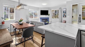 Una cocina moderna con una isla grande, un comedor con mesa y sillas de madera, y un sofá gris.