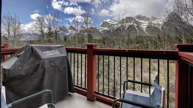 A balcony with a barbecue grill, a chair, and a view of snow-capped mountains. - C303 Peaceful Canmore Corner- Downtown, Free parking, View, 2BR, 2BT, Sleeps 7 (Canmore)