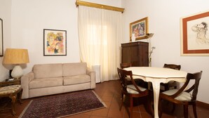 Un salon comprenant un canapé, une table à manger avec des chaises, un tapis à motifs et des œuvres d’art accrochées aux murs.