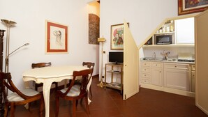 Un coin repas avec une table et des chaises, un téléviseur posé sur un meuble, et un espace cuisine équipé de placards et d’un four à micro-ondes.