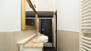 Une petite salle de bain avec un lavabo blanc, un miroir à cadre doré et une cabine de douche noire.