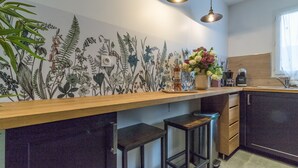 A kitchen with a wooden countertop, two bar stools, a wall-mounted light fixture, and a window with curtains.