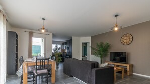 A modern living room with a dining area, a sofa, a TV, and a clock on the wall.