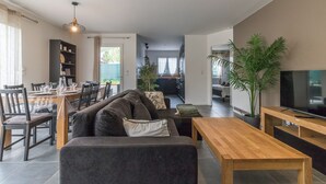 A modern living room with a sofa, dining table, and chairs, a wooden coffee table, and a television.