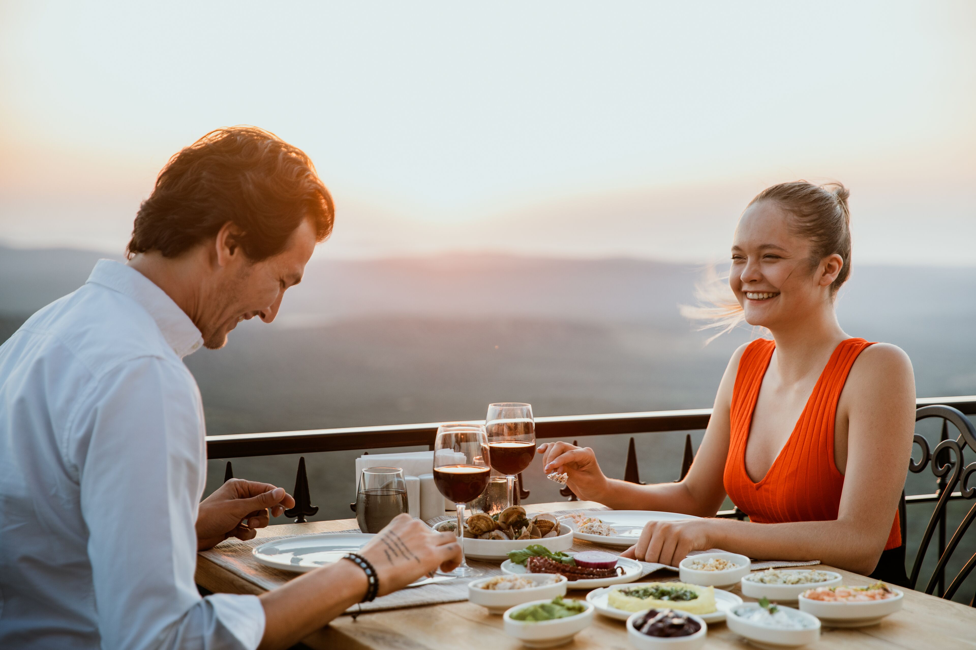 Una pareja cenando en una mesa con vistas panorámicas, platos de comida y copas de vino.