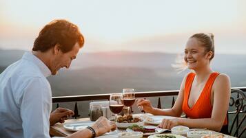 Una pareja cenando en una mesa con vistas panorámicas, platos de comida y copas de vino.