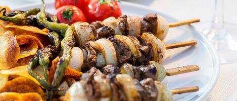 Un plato con brochetas de carne y verduras, una copa de vino tinto y un bol de ensalada.