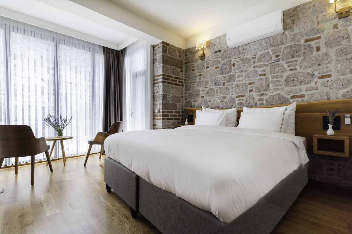 A bedroom with a large bed, a stone accent wall, a wooden nightstand, and a small table with chairs.
