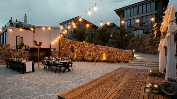 Un área de comedor al aire libre con muros de piedra, cubierta de madera y luces colgantes.