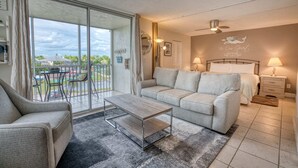A modern hotel room with a sofa, a coffee table, a bed, and a balcony with a view of the outdoors. - Beautiful Beach Studio at Beach And Tennis 3304 (Bonita Springs)