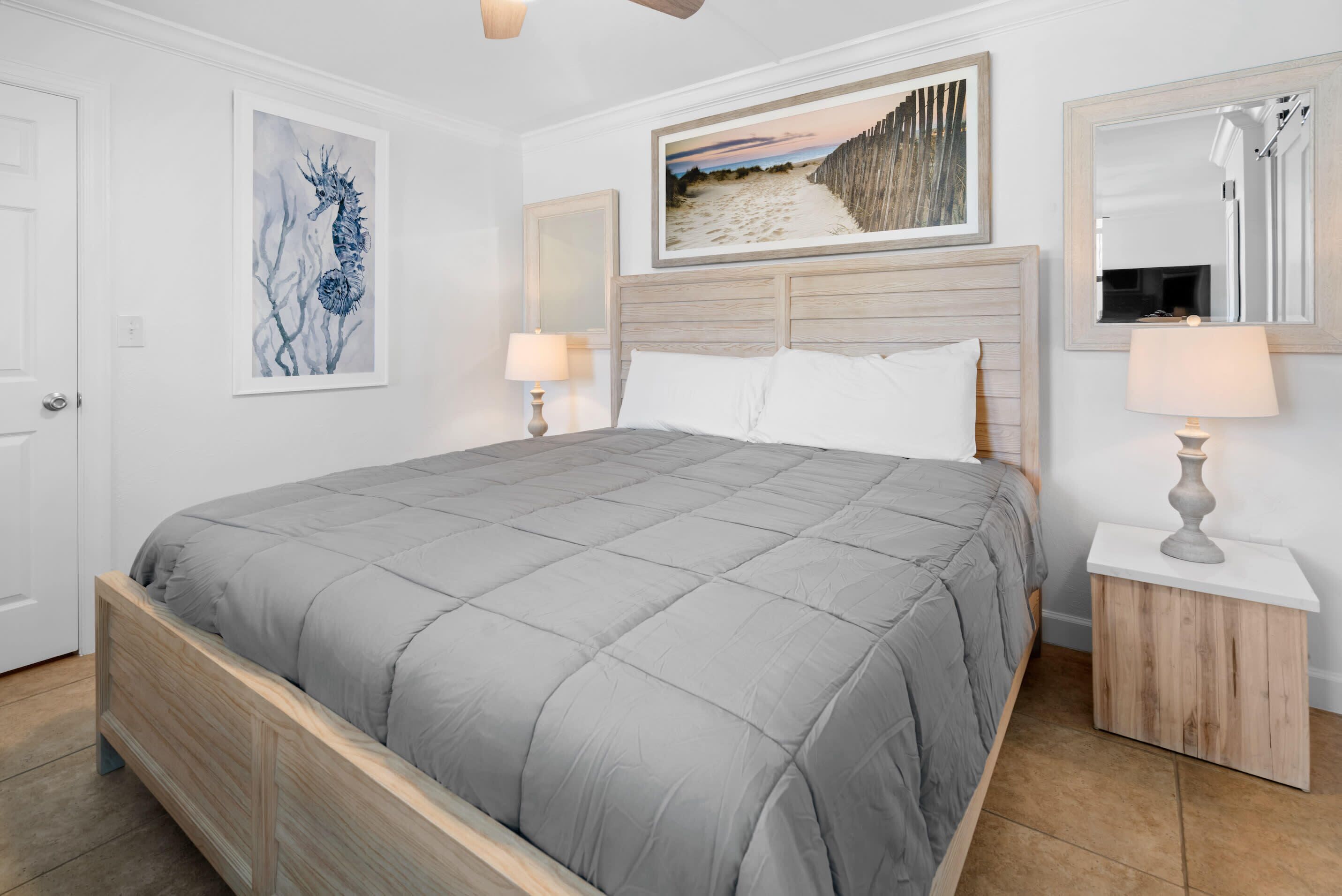 A neatly arranged bedroom with a large bed, a wooden headboard, a bedside table with a lamp, and artwork on the walls.