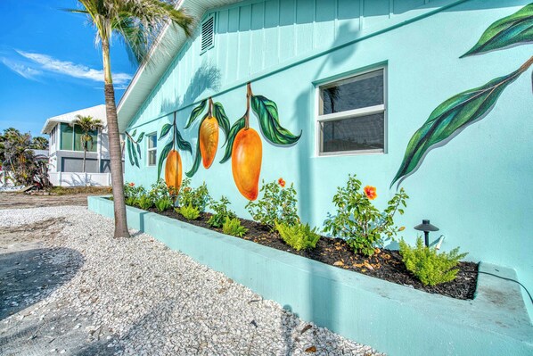A house with a light blue exterior and a mural of mangoes and leaves.