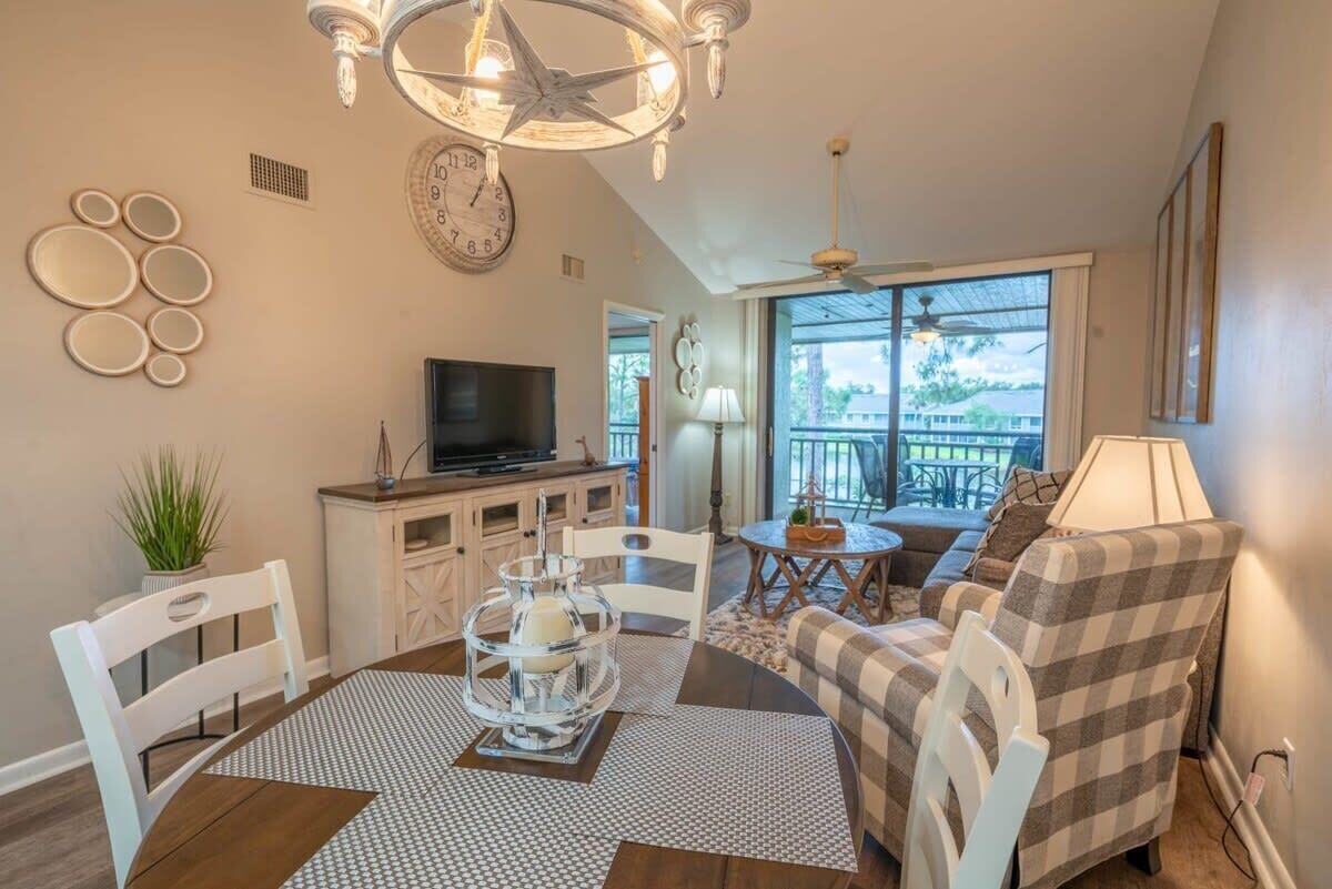 Un salon confortable avec un téléviseur, une table à manger et des chaises, un balcon avec vue et un ventilateur de plafond.