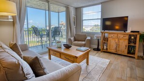 A living room with a sofa, coffee table, TV, and a balcony with outdoor furniture.