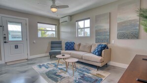 A living room with a beige sofa, two side tables, a ceiling fan, and artwork on the walls. - Mango Street Inn Suite 5 (Fort Myers Beach)