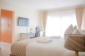 Habitación de hotel con cama, escritorio, televisor y ventana con cortinas.