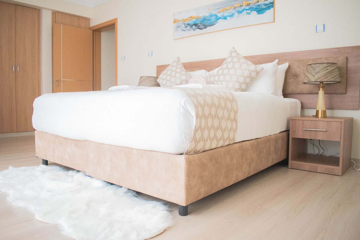 Un dormitorio con cama, mesita de noche, lámpara, un cuadro y un armario de madera.