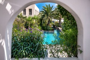 Une piscine entourée d’une végétation luxuriante et surmontée d’une arche blanche.